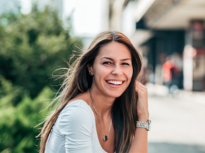 Woman with watch and long hair standing outside smiling