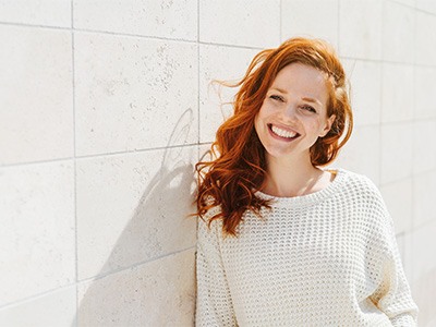 Woman in white sweater leaning against wall and smiling