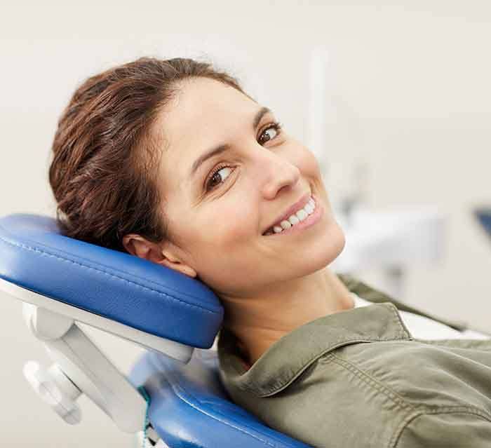 Woman in green shirt with brown hair in blue dental chair smiling