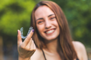 Woman holding up an Invisalign tray and smiling